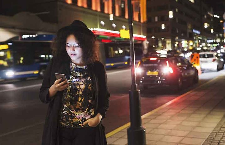 Kvinna med mobil i trafikmiljö under kvällen