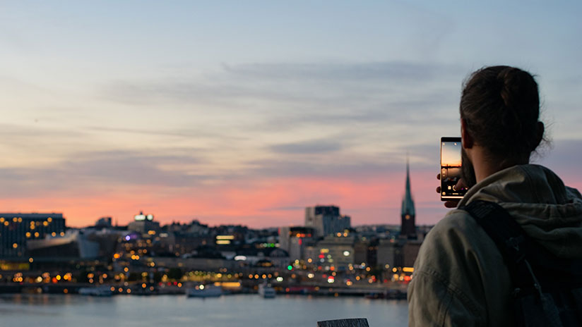 Ung man med mobil fotar kvällsbild över Stockholm